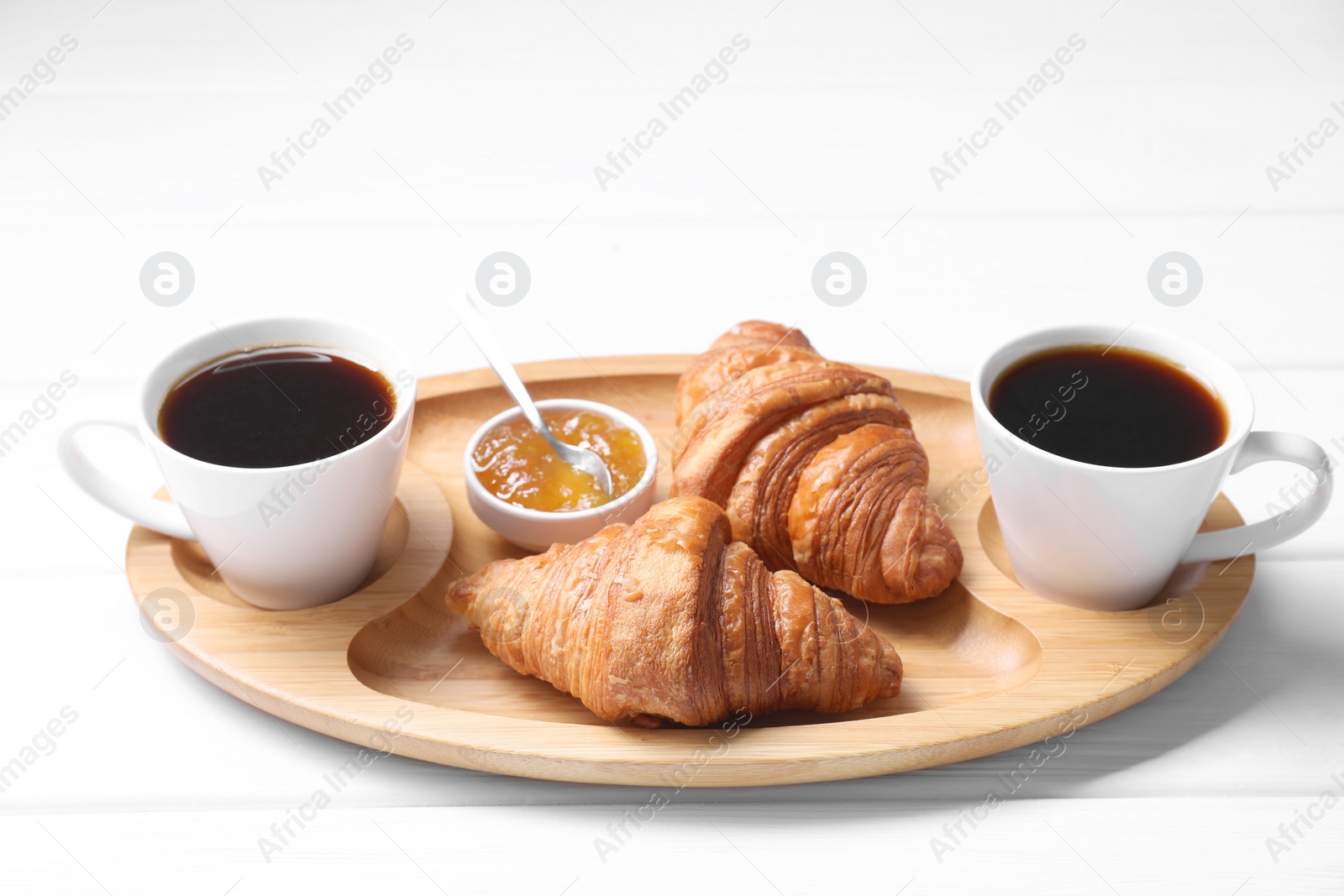 Photo of Tasty breakfast. Cups of coffee, jam and croissants on white wooden table