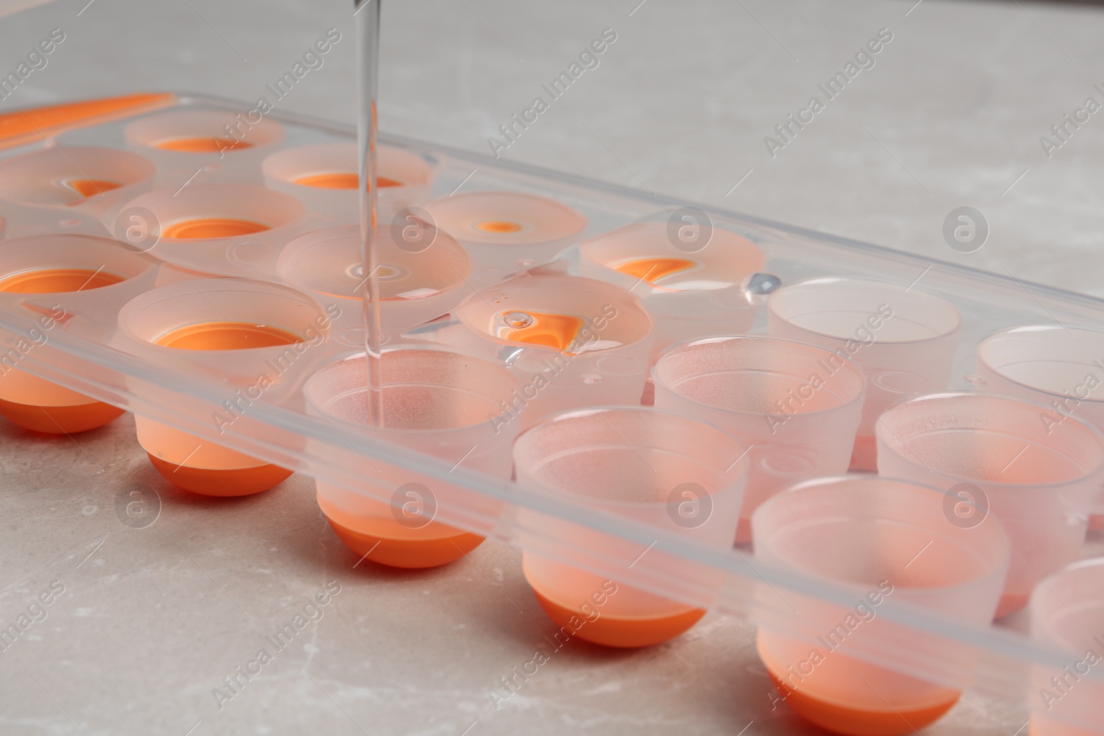 Photo of Pouring water into ice cube tray on table, closeup