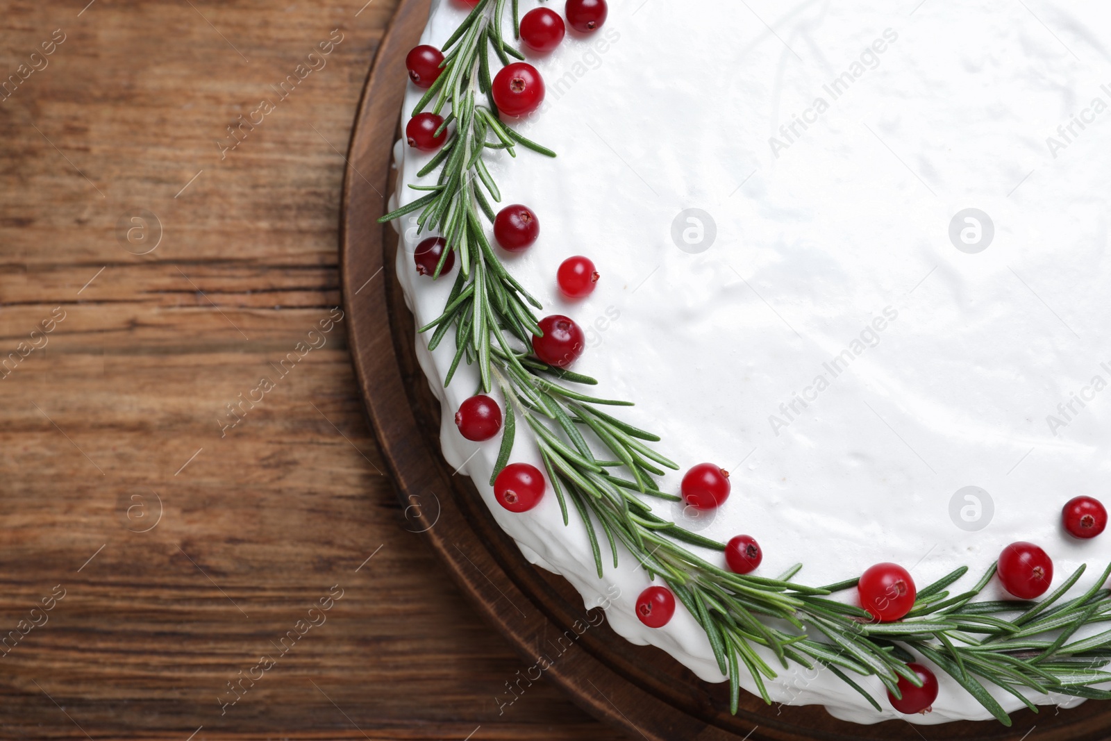 Photo of Traditional Christmas cake decorated with rosemary and cranberries on wooden table, top view