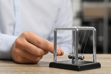 Photo of Man playing with Newton's cradle at wooden table, closeup. Physics law of energy conservation