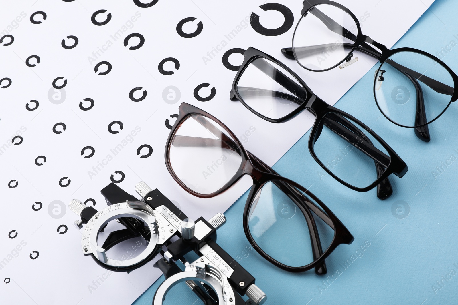 Photo of Vision test chart, glasses and trial frame on light blue background