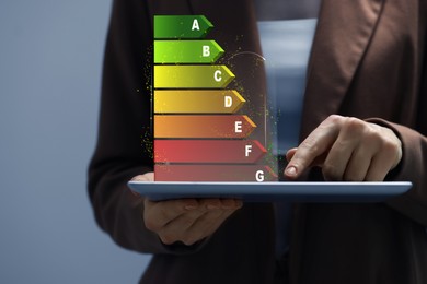 Image of Energy efficiency rating coming out of tablet. Man using device on grey background, closeup