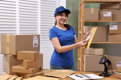 Photo of Parcel packing. Post office worker sticking barcode on bag at wooden table indoors