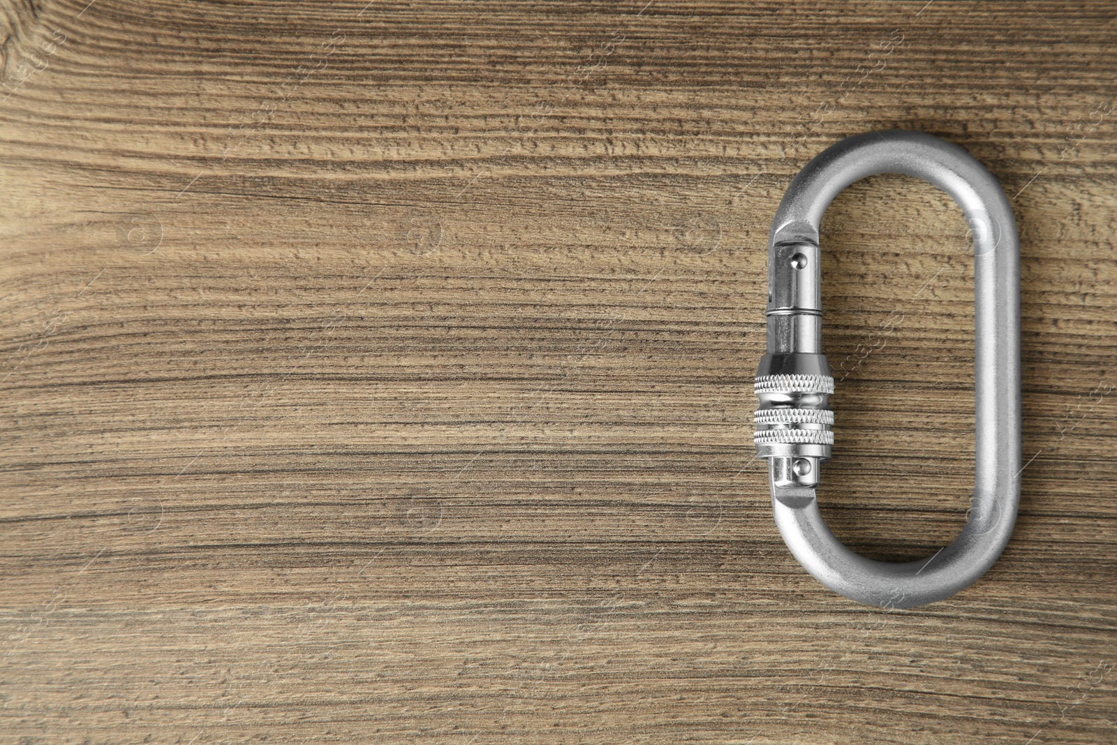 Photo of One metal carabiner on wooden table, top view. Space for text