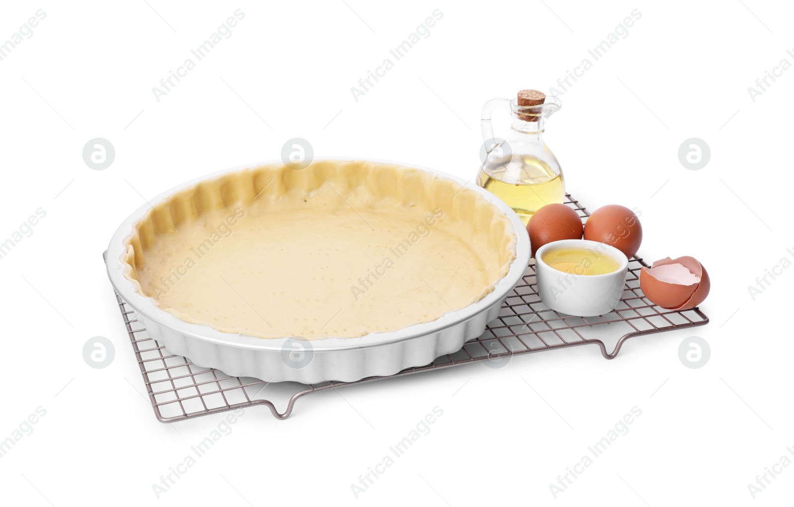 Photo of Quiche pan with fresh dough, oil and eggs isolated on white
