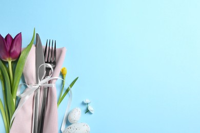 Photo of Cutlery set, Easter eggs and beautiful flowers on light blue background, flat lay with space for text. Festive table setting