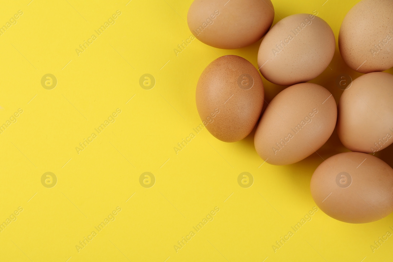 Photo of Raw chicken eggs on yellow background, flat lay. Space for text