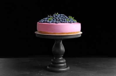 Stand with tasty blueberry cake on table against black background