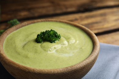 Photo of Wooden bowl of delicious broccoli cream soup on table, closeup