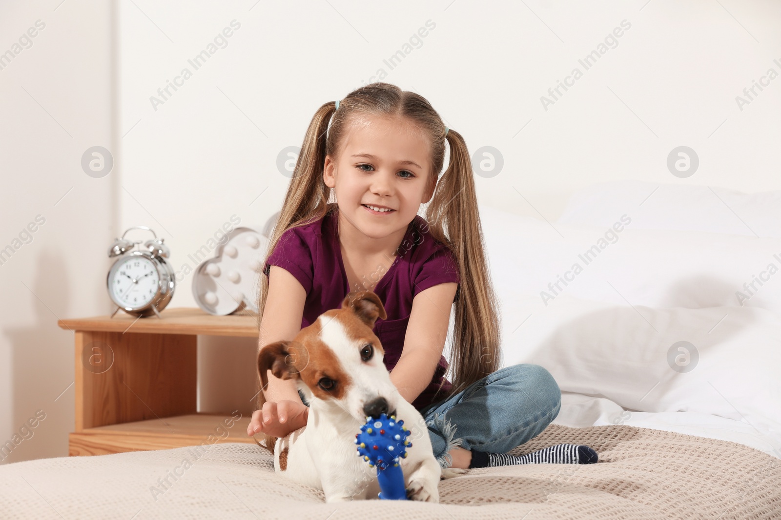 Photo of Cute girl with her playful dog on bed at home. Adorable pet