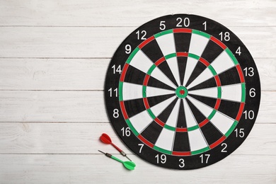 Dart board with color arrows on white wooden background, top view. Space for text