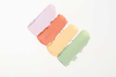 Photo of Samples of different color correcting concealers on white background, top view