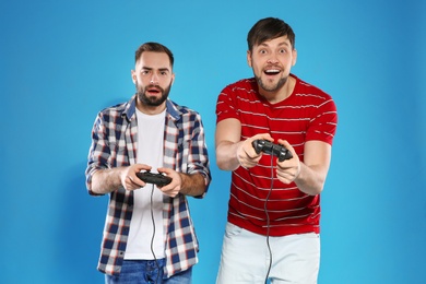 Emotional men playing video games with controllers on color background