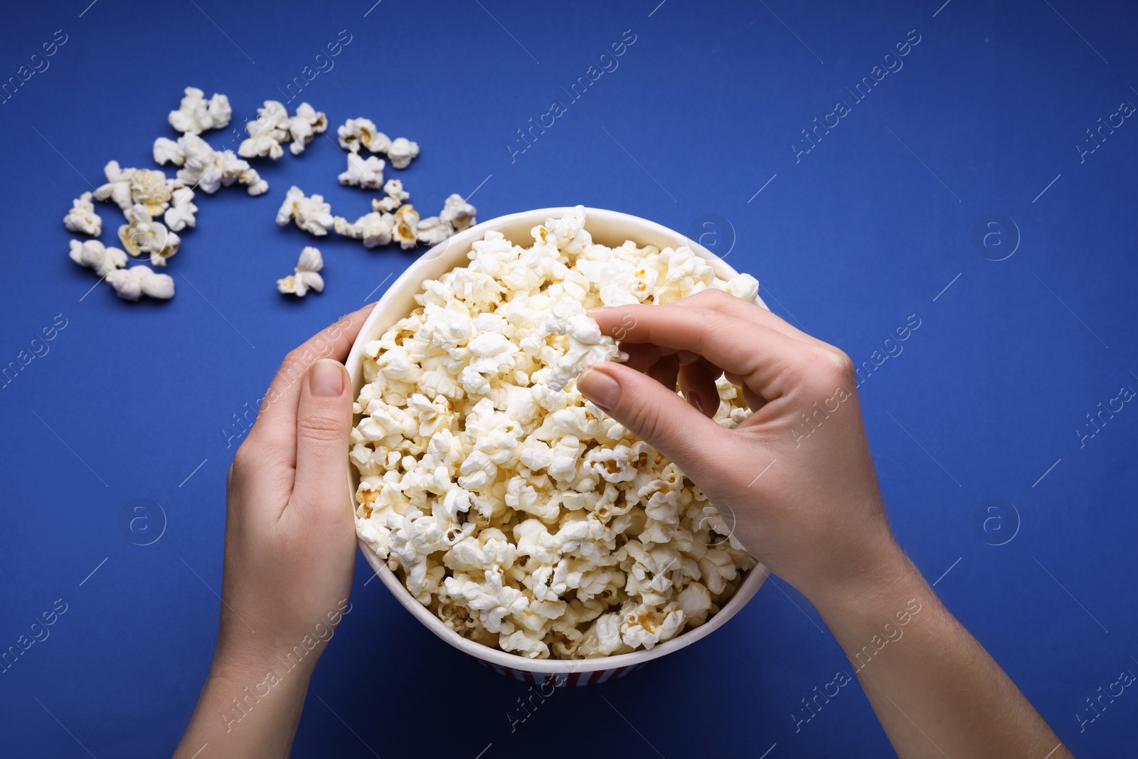 Photo of Woman taking fresh popcorn from bucket on blue background, above view