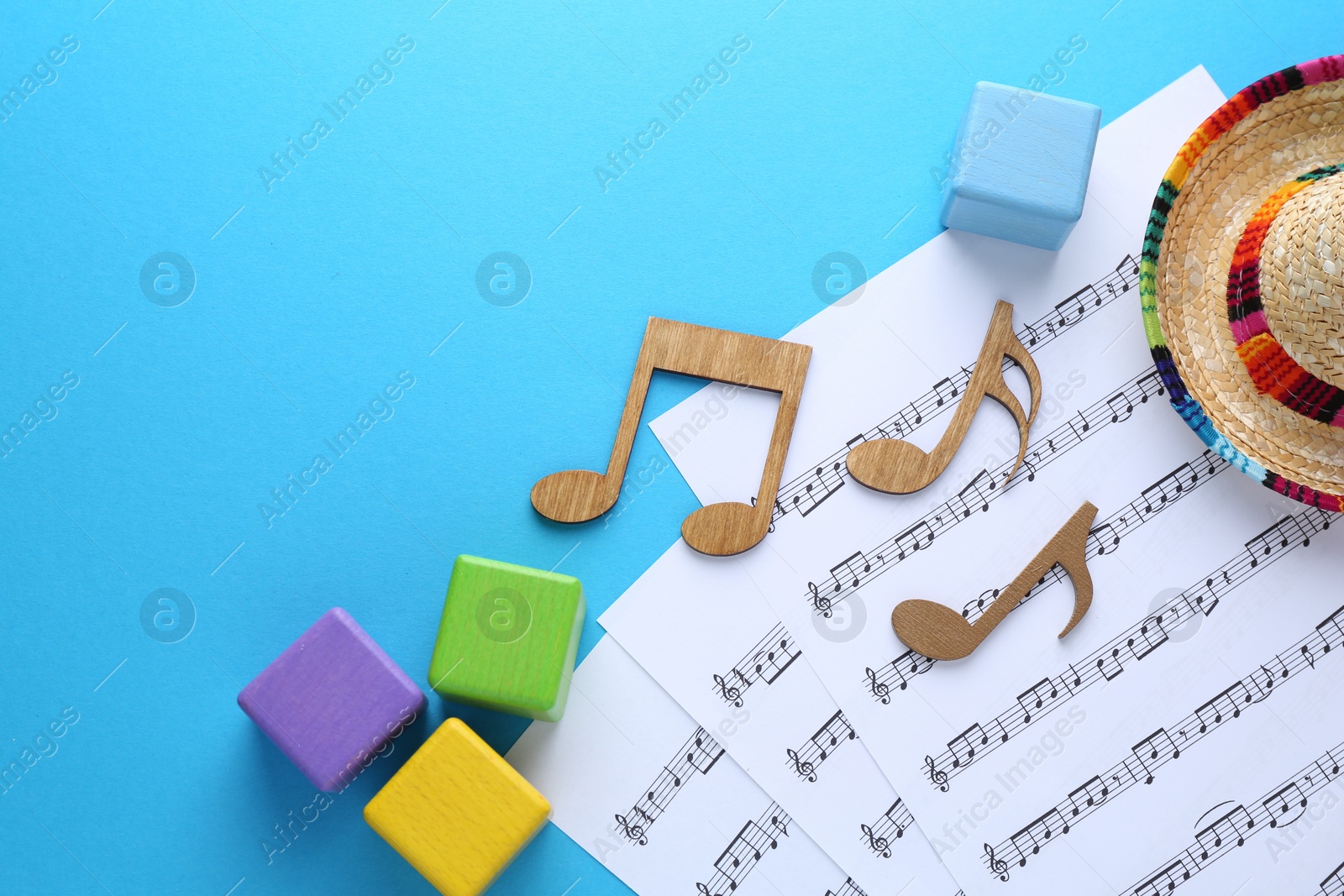 Photo of Baby songs. Music sheets, wooden notes, cubes and hat on light blue background, flat lay with space for text