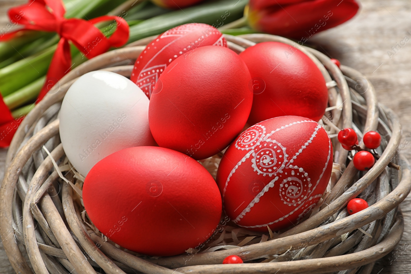 Photo of Wicker nest with painted Easter eggs on table, closeup