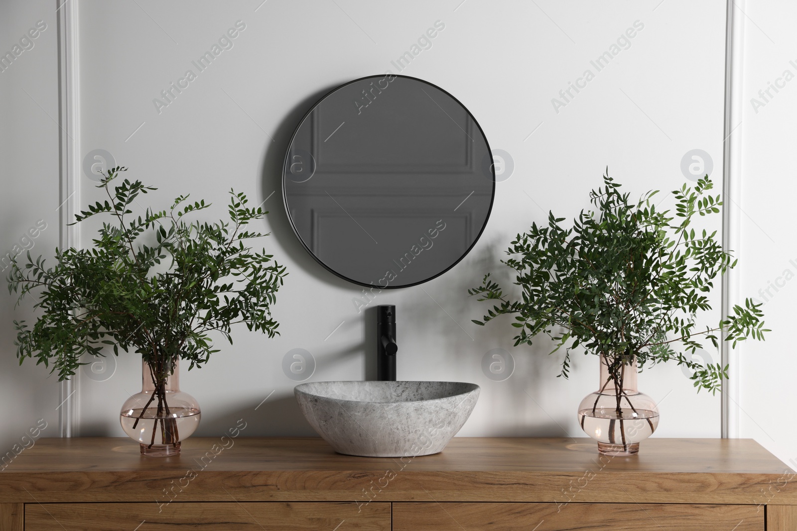 Photo of Eucalyptus branches near vessel sink on bathroom vanity. Interior design