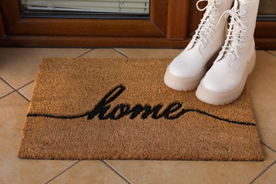 Doormat with word Home and stylish boots near entrance outdoors