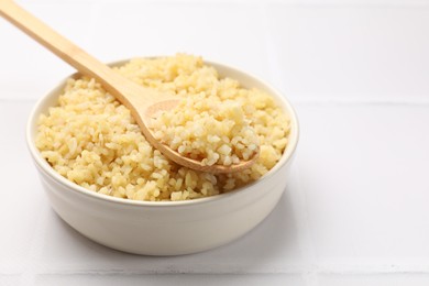 Photo of Delicious bulgur served on white tiled table, closeup. Space for text