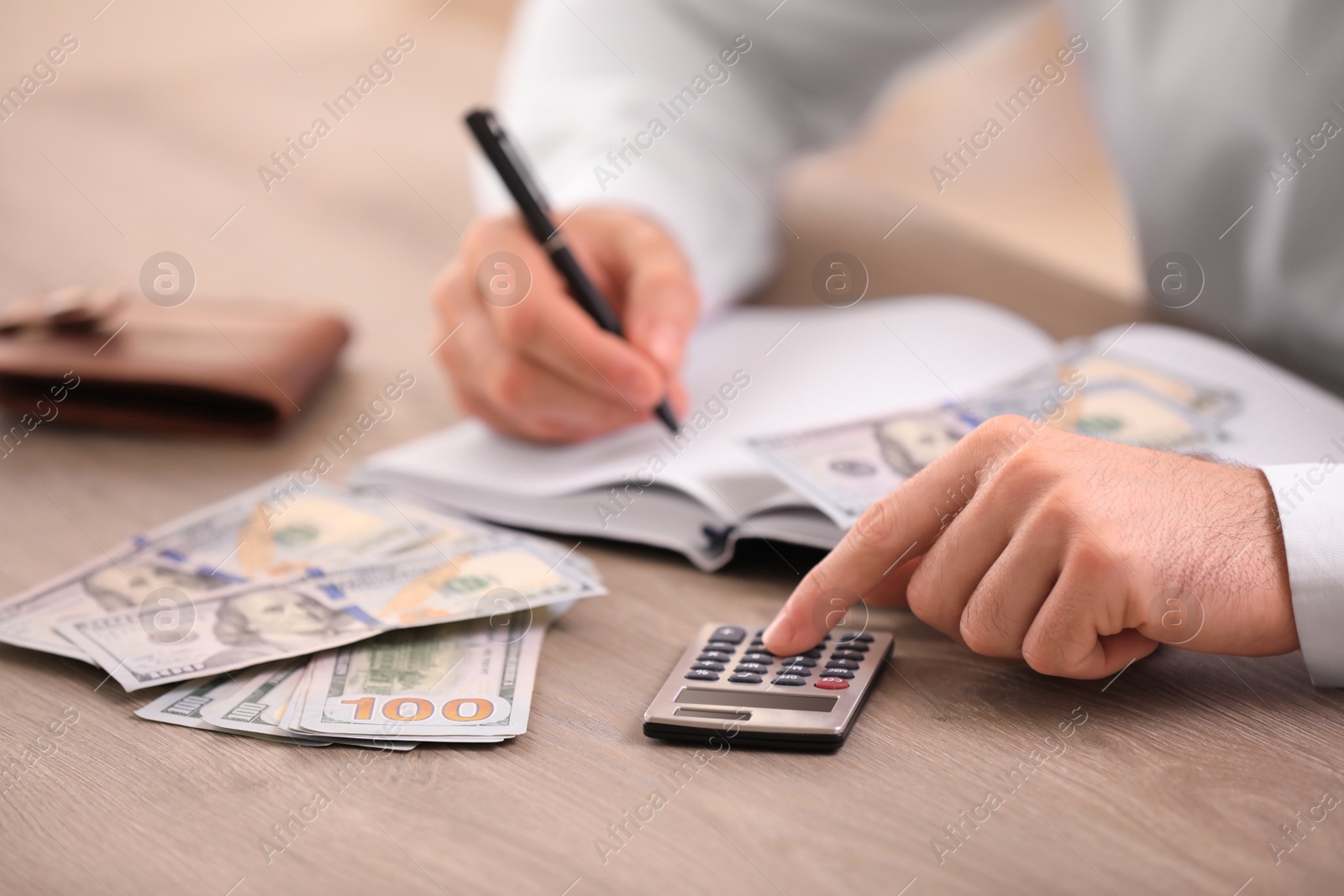 Photo of Man with dollar bills and calculator at wooden table, closeup