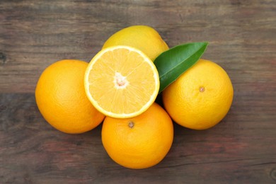 Photo of Many ripe oranges and green leaf on wooden table, flat lay