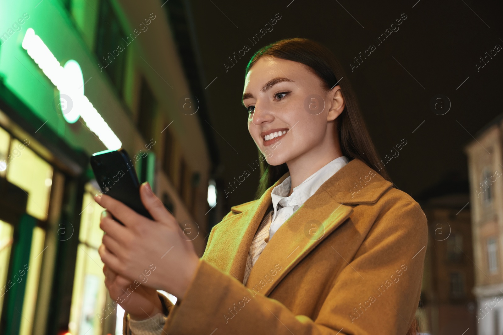 Photo of Smiling woman using smartphone on night city street