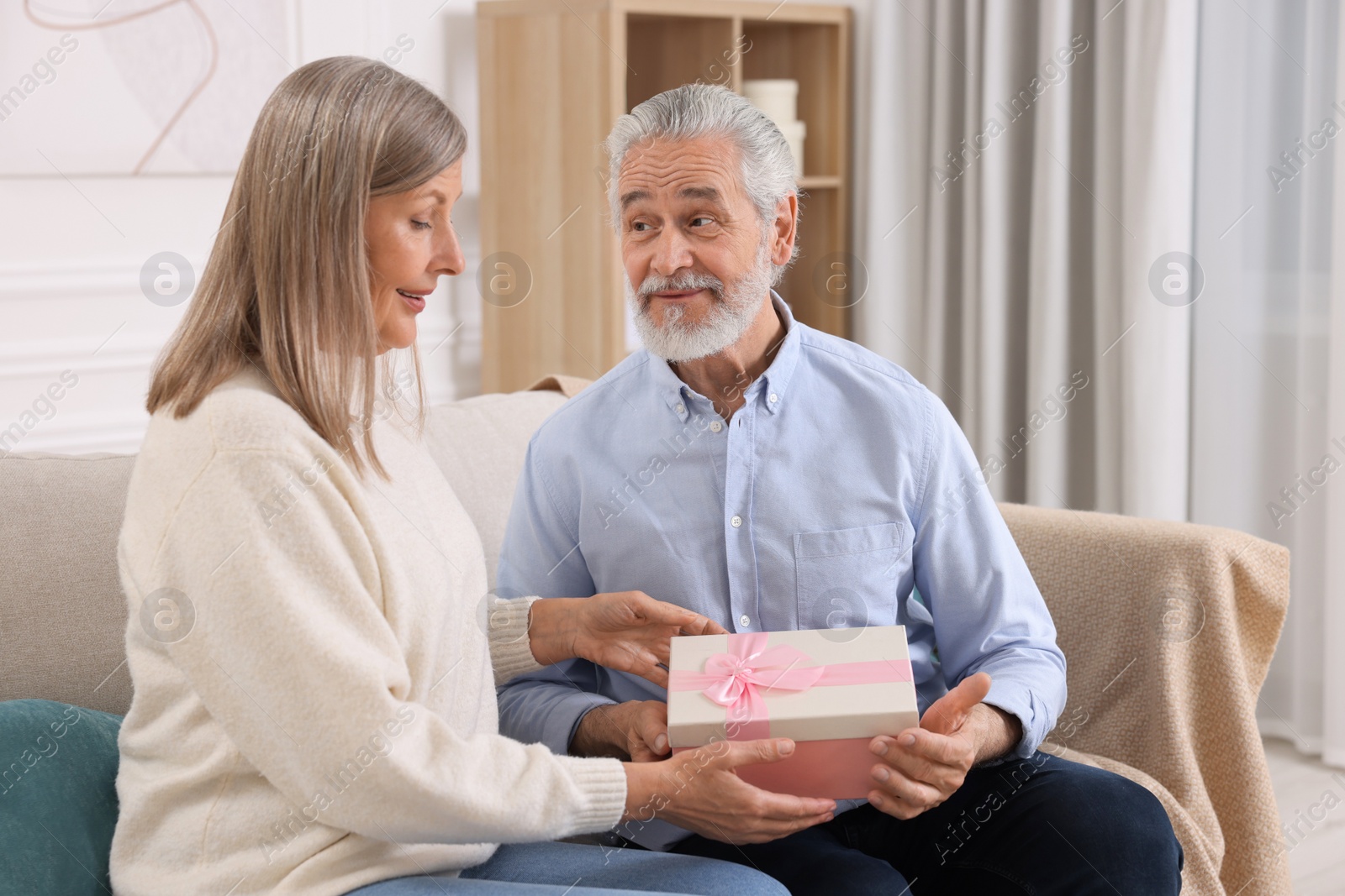Photo of Happy affectionate senior couple with gift box on sofa indoors