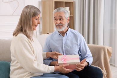 Happy affectionate senior couple with gift box on sofa indoors