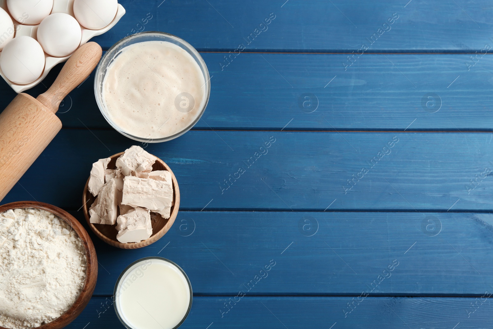 Photo of Pieces of compressed yeast and dough ingredients on blue wooden table, flat lay. Space for text