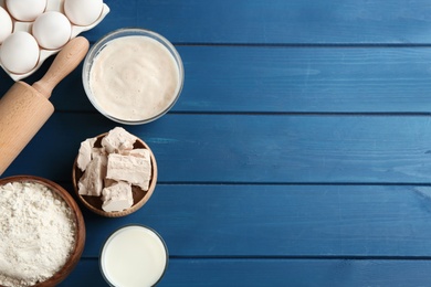 Photo of Pieces of compressed yeast and dough ingredients on blue wooden table, flat lay. Space for text