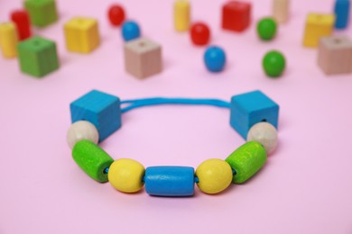 Wooden pieces and string for threading activity on pink background, closeup. Educational toy for motor skills development