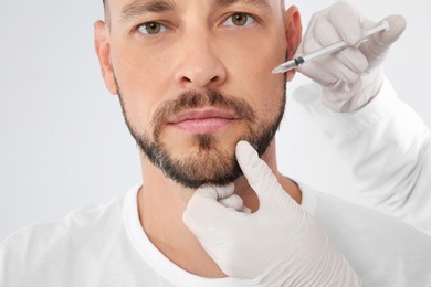 Photo of Man getting facial injection on white background, closeup. Cosmetic surgery concept
