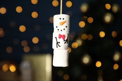 Funny snowman made of marshmallows against blurred festive lights, closeup