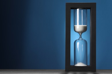 Hourglass with flowing sand on table against blue background, space for text