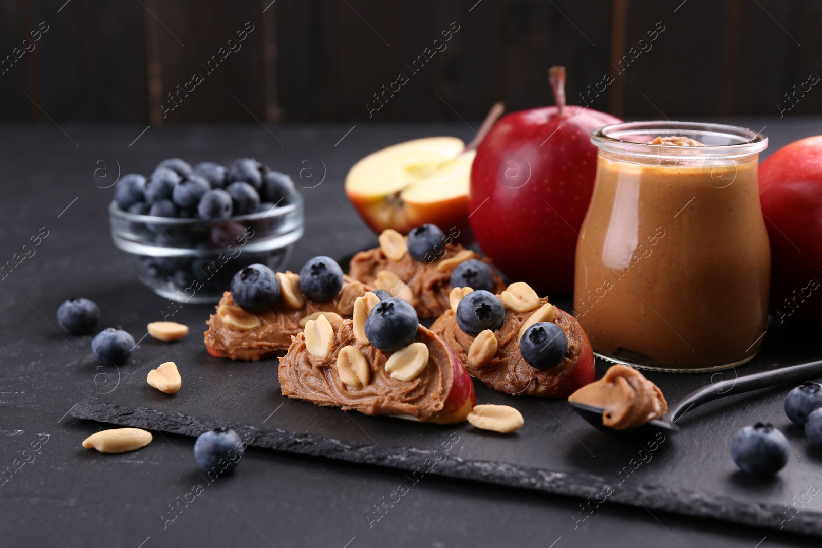Photo of Fresh apples with peanut butter and blueberries on dark table