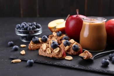 Photo of Fresh apples with peanut butter and blueberries on dark table