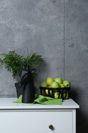 Photo of Stylish decor, basket with apples and houseplant on chest of drawers near grey wall indoors, space for text. Interior design