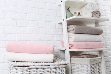 Photo of Shelving unit and baskets with clean towels and toiletries near brick wall