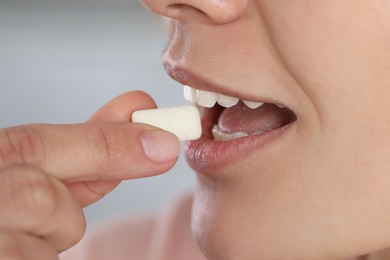Photo of Woman putting chewing gum into mouth on blurred background, closeup