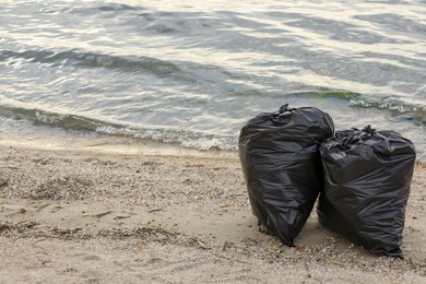 Photo of Trash bags full of garbage on beach. Space for text