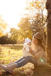 Photo of Happy mother with her baby daughter sitting near tree in park on sunny autumn day, space for text