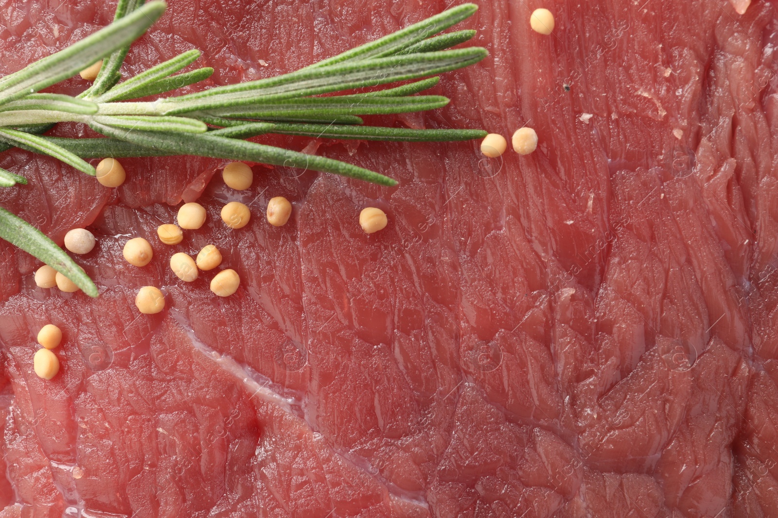 Photo of Piece of raw beef meat with spices and rosemary as background, top view