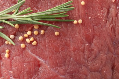 Piece of raw beef meat with spices and rosemary as background, top view