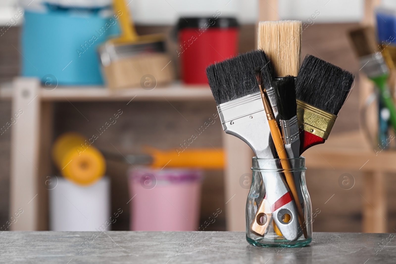 Photo of Glass jar with paint brushes on table in workshop. Space for text