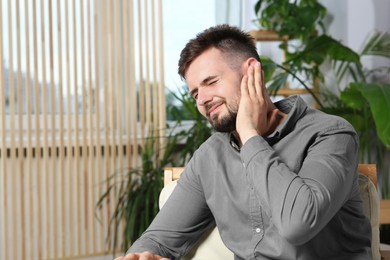 Photo of Young man suffering from ear pain at home. Space for text