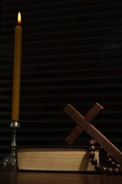 Church candle, Bible, cross and rosary beads on wooden table