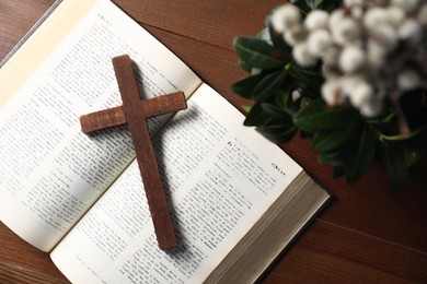 Bible, plant with willow branches and cross on wooden table, flat lay