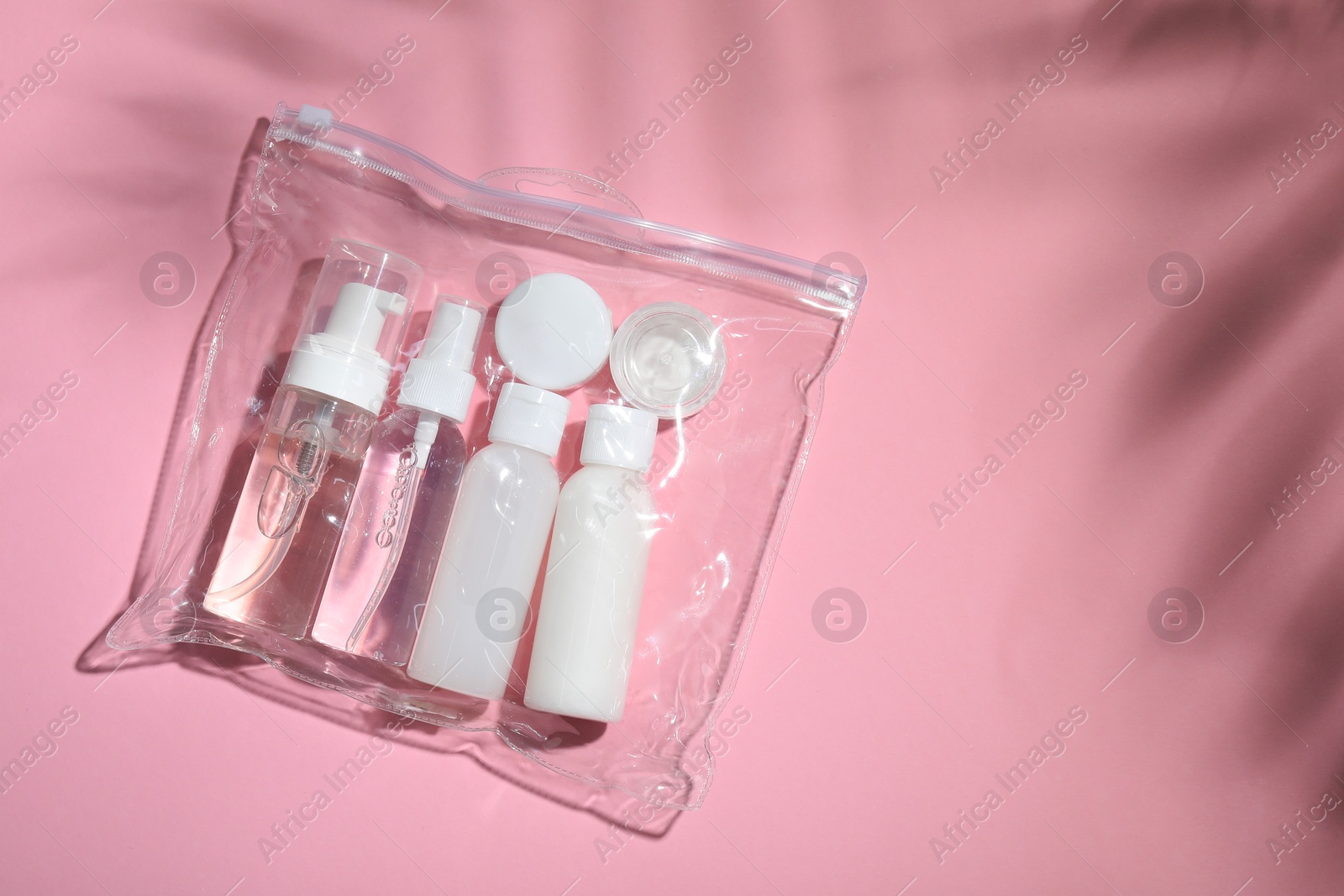 Photo of Cosmetic travel kit in plastic bag on pink background, top view and space for text. Bath accessories