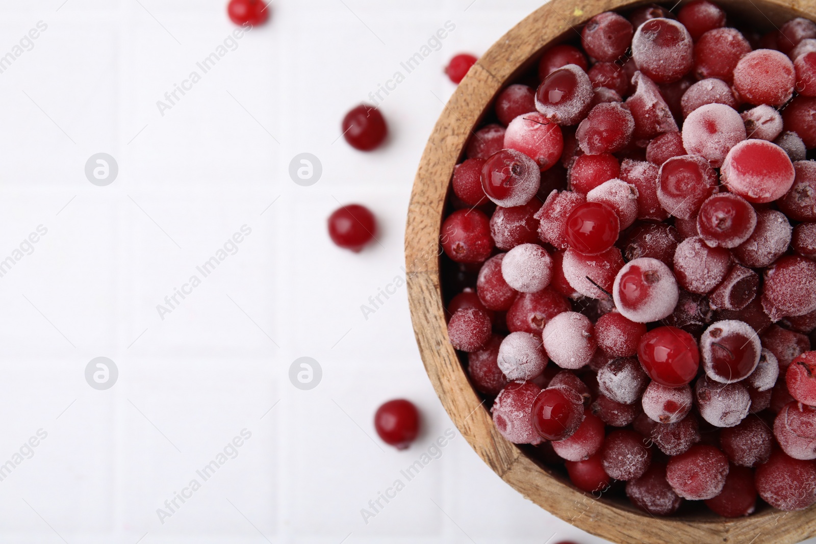 Photo of Frozen red cranberries in bowl on white tiled table, top view. Space for text