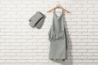 Photo of Clean kitchen apron with pattern and oven gloves on white brick wall. Space for text